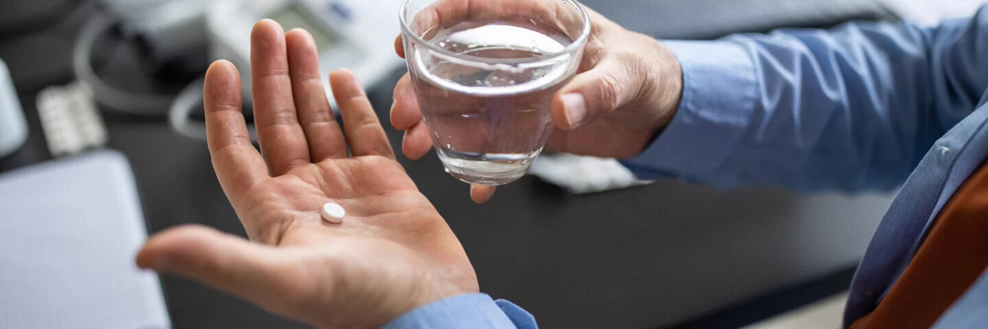 Ein Mann hält eine Schmerztablette und ein Glas Wasser in der Hand.