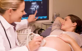 Eine schwangere Frau blickt mit ihrer Ärztin auf Ergebnisse der Ultraschall-Untersuchung