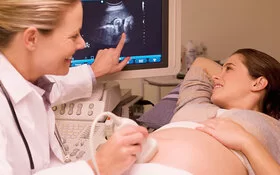 Eine schwangere Frau blickt mit ihrer Ärztin auf Ergebnisse der Ultraschall-Untersuchung