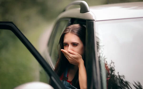 Eine junge Frau leidet unter Reiseübelkeit und steigt aus dem Auto aus.