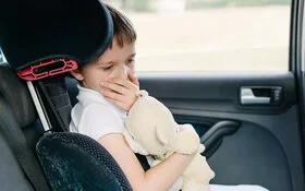 Ein Junge sitzt auf der Rückbank eines Autos. Ihm ist übel. Er hält eine Hand vor den Mund und umklammert sein Stofftier.