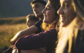 Eine Gruppe jugendlicher Wanderer sitzt auf einer Wiese und schaut in die Ferne.