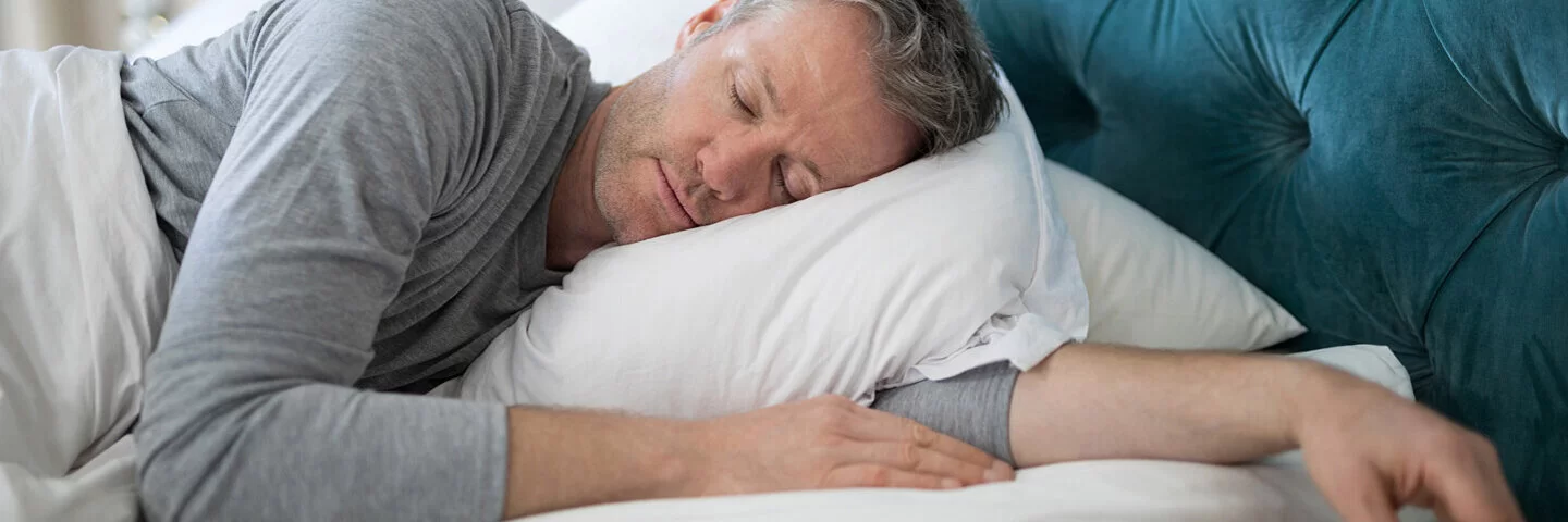 Mann liegt entspannt im Bett und schläft.