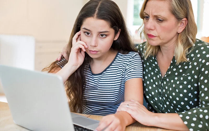 Eine Mutter und Tochter sitzen am Laptop und sprechen über Cybermobbing.