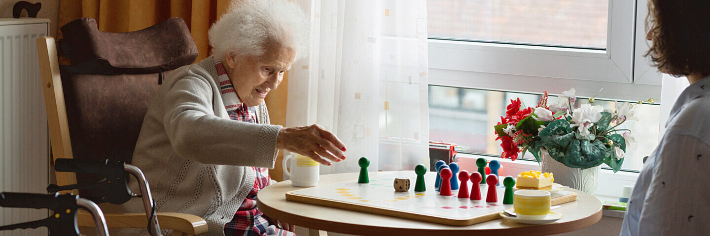 Frau im FSJ spielt mit einer älteren Dame eine Brettspiel.