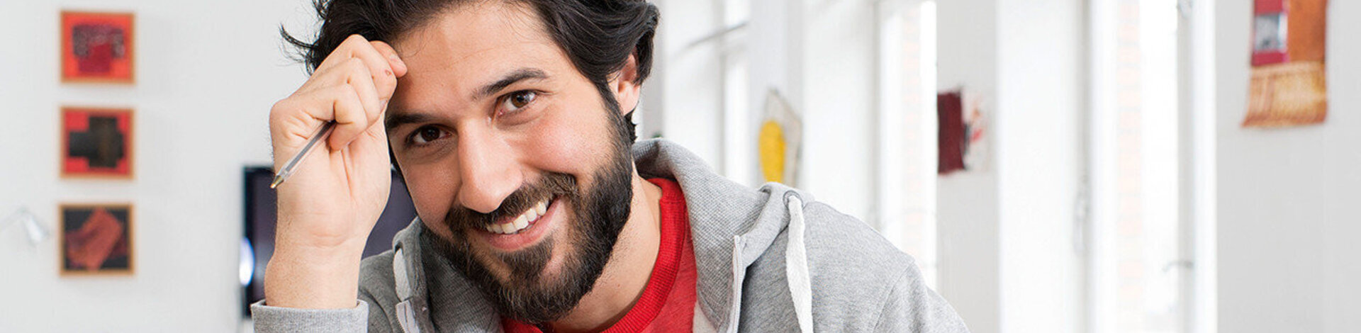 A man smiles and holds a pen in his hand. Find information in your language.