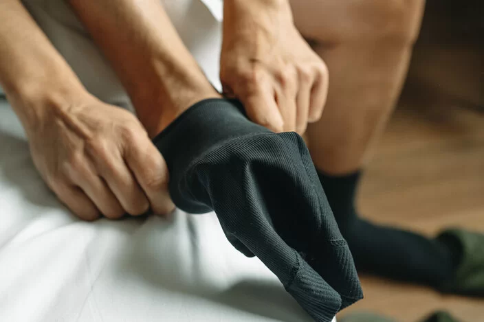 Ein Mann sitzt auf seinem Bett und zieht Kompressionsstrümpfe über seine Füße.