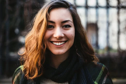 Junge Frau mit wenigen Muttermalen im Gesicht lächelt in die Kamera.