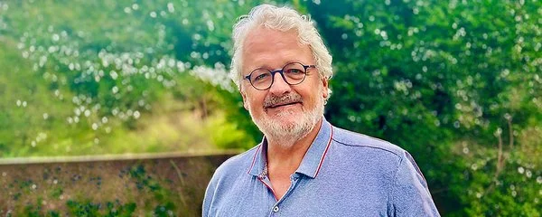 Prof. Dr. Thomas Schläpfer trägt ein Poloshirt und steht in einem sonnigen Garten.
