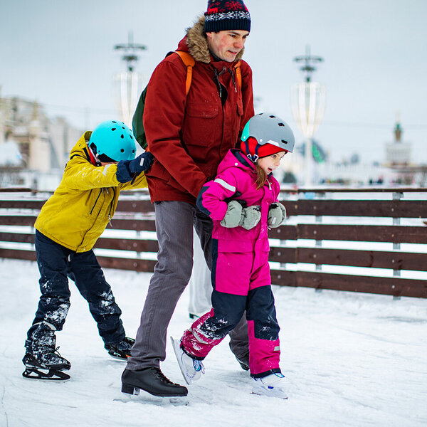 Ein Vater beim Schlittschuhlaufen mit seinen zwei kleinen Kindern.