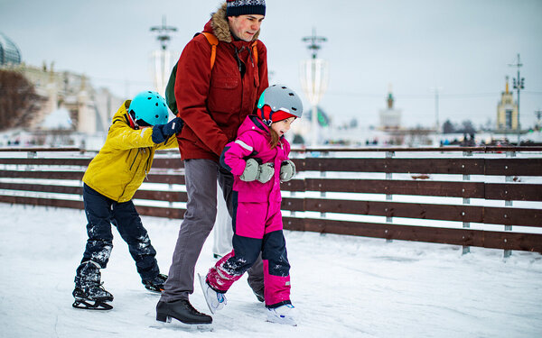 Ein Vater beim Schlittschuhlaufen mit seinen zwei kleinen Kindern.