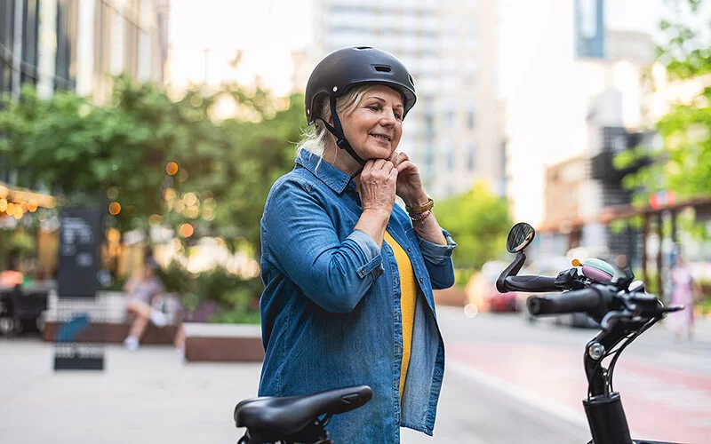Eine Frau steht neben ihrem Fahrrad. Sie hat einen Fahrradhelm auf dem Kopf und verschließt ihn sorgfältig.