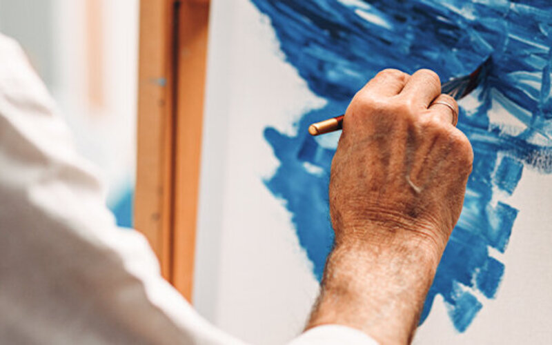 Mann malt ein Bild auf einer Staffelei mit der Farbe Blau. 