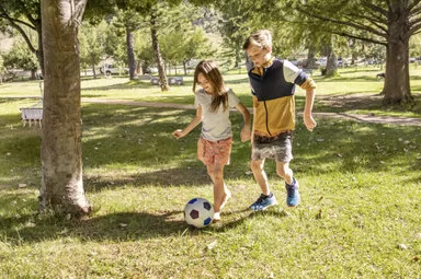 Mädchen und Junge spielen Fußball im Park. Mit dem AOK-Kinderbonus können sie bei der Teilnahme an Gesundheitskursen Punkte sammeln und eine Prämie erhalten.