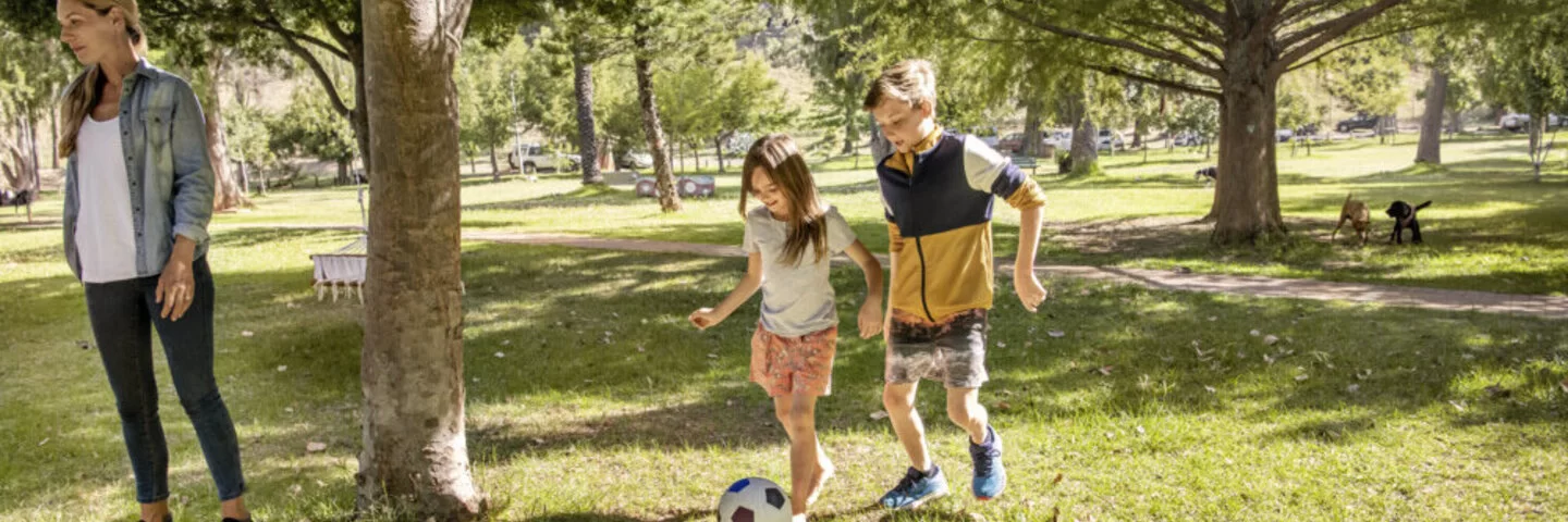 Mädchen und Junge spielen Fußball im Park. Mit dem AOK-Kinderbonus können sie bei der Teilnahme an Gesundheitskursen Punkte sammeln und eine Prämie erhalten.