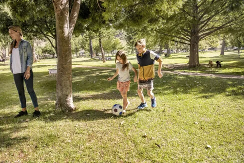 Mädchen und Junge spielen Fußball im Park. Mit dem AOK-Kinderbonus können sie bei der Teilnahme an Gesundheitskursen Punkte sammeln und eine Prämie erhalten.