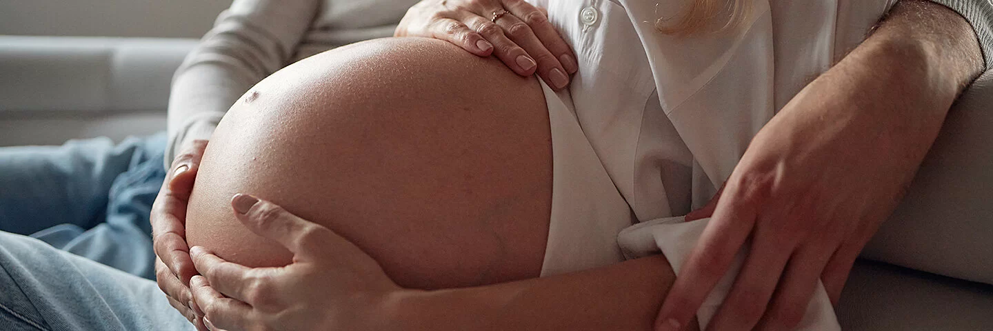 Schwangere Frau streichelt ihren Babybauch, ihr Partner legt den Arm um sie.