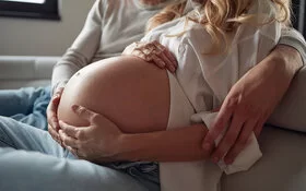 Schwangere Frau streichelt ihren Babybauch, ihr Partner legt den Arm um sie.