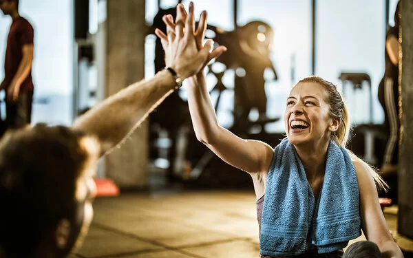 Frau klatscht ihren Partner im Fitnessstudio ab, weil sich nach und nach ihre SMART-Ziele erreicht.