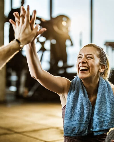 Frau klatscht ihren Partner im Fitnessstudio ab, weil sich nach und nach ihre SMART-Ziele erreicht.