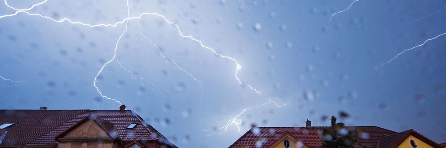 Eine Häuserfront bei starkem Unwetter mit Blitzen am Himmel.