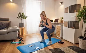 Eine Frau trainiert zu Hause in ihrem Wohnzimmer mit einer Kettlebell.