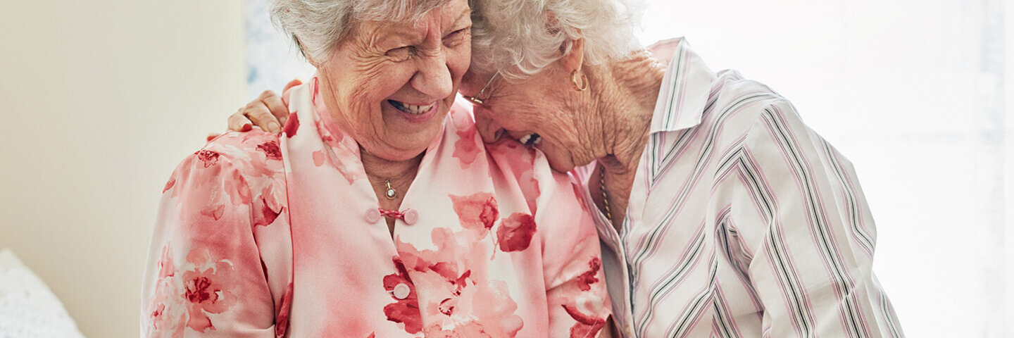 Neue Freunde finden: Zwei Frauen sitzen nebeneinander und freuen sich, weil sie im Alter zueinander gefunden haben.