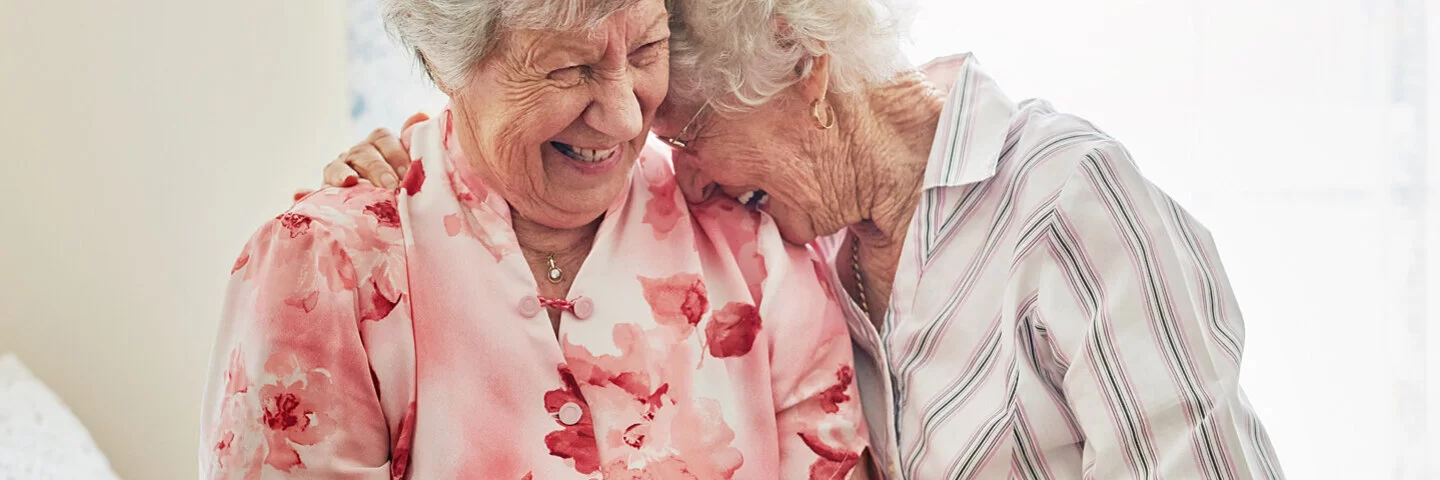 Neue Freunde finden: Zwei Frauen sitzen nebeneinander und freuen sich, weil sie im Alter zueinander gefunden haben.