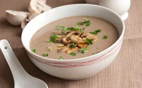 Cremige Pilzsuppe mit Champignons garniert mit gehackter Petersilie in einer weißen Suppenschüssel serviert.