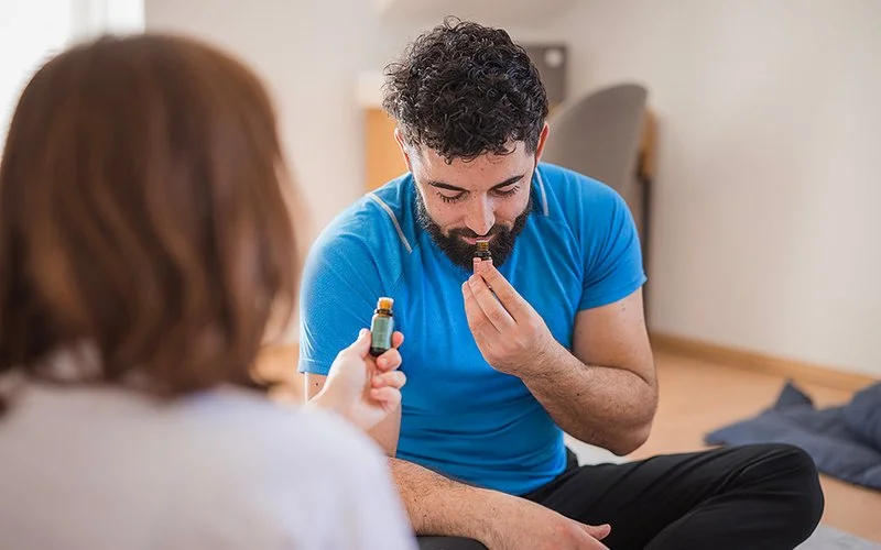 Ein Mann sitzt auf einem Boden und riecht an einem kleinen Fläschchen.