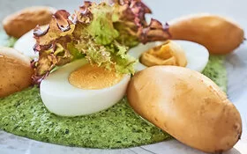 Eine Portion grüne Soße mit Kartoffeln und halben Eiern liegt auf einem weißen Teller.