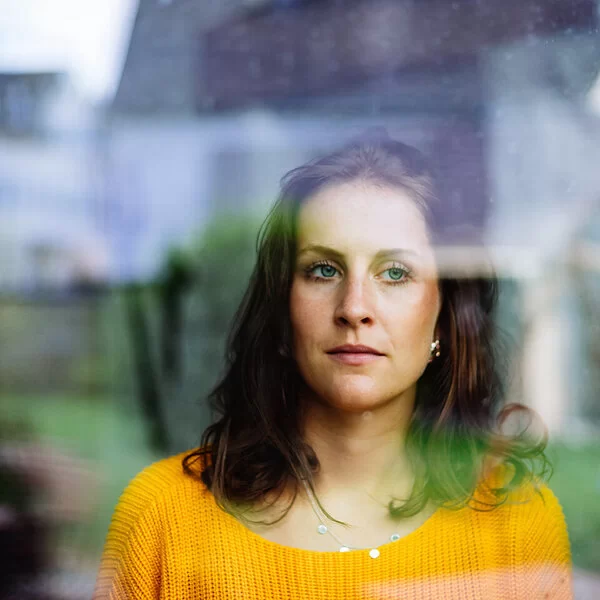 Symbolbild für Autismus bei Frauen: Hinter einer Fensterscheibe steht eine Frau ,die nachdenklich nach draußen schaut.