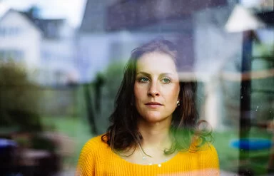 Symbolbild für Autismus bei Frauen: Hinter einer Fensterscheibe steht eine Frau ,die nachdenklich nach draußen schaut.