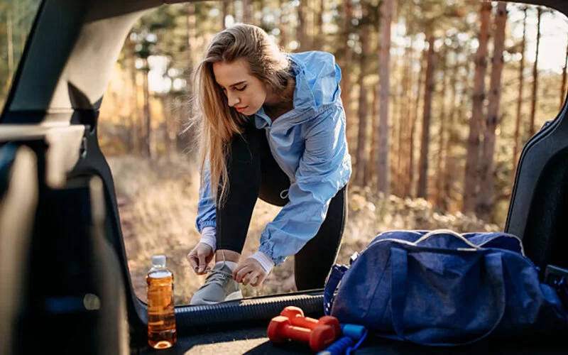 Eine Frau bindet sich an ihrem Auto im Wald die Laufschuhe zu.