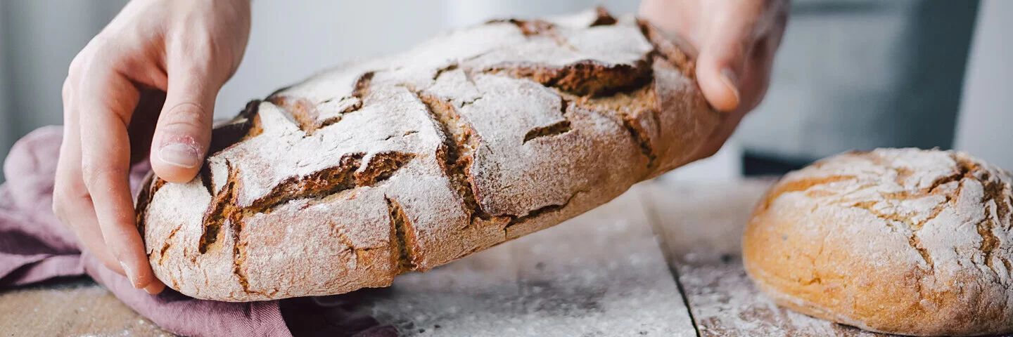 Mann hält selbstgebackenes Sauerteigbrot.