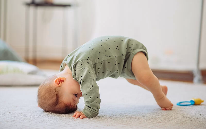 Baby lernt laufen und versucht allein aufzustehen, indem es sich mit dem Kopf vom Boden hochschiebt.