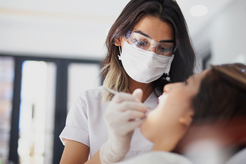 Eine Zahnärztin mit Mundschutz und Brille hält ein Behandlungsinstrument an das Gebiss einer Patientin. Die AOK-Zahnklinik bietet sämtliche Behandlungen an.