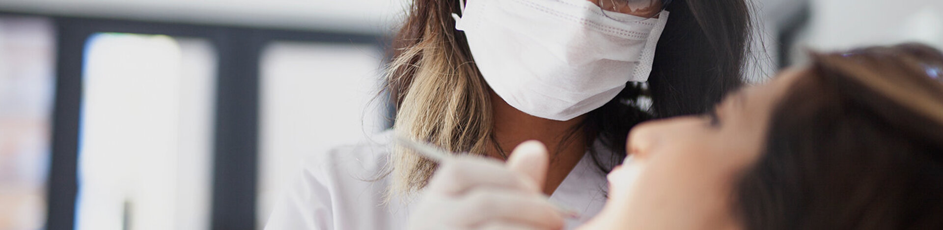 Eine Zahnärztin mit Mundschutz und Brille hält ein Behandlungsinstrument an das Gebiss einer Patientin. Die AOK-Zahnklinik bietet sämtliche Behandlungen an.