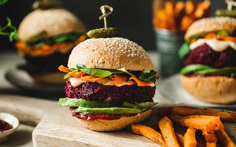 Ein Burger mit Gemüse-Patty auf einem Holzbrett, angerichtet mit Süßkartoffel-Pommes.