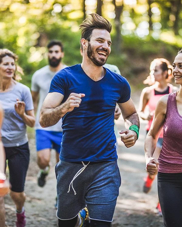 Ein Gruppe fröhlicher Menschen läuft in Sportkleidung durch einen Wald.