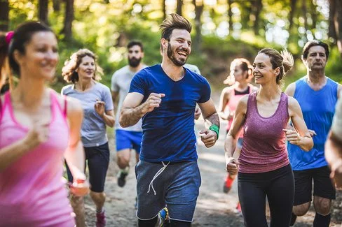 Ein Gruppe fröhlicher Menschen läuft in Sportkleidung durch einen Wald.