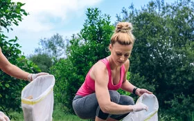 Zwei Frauen laufen draußen mit Müllsäcken umher und machen Plogging