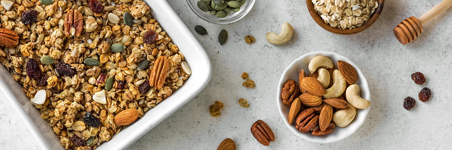 Selbst gemachtes Granola, daneben Zutaten wie Nüsse und Haferflocken.