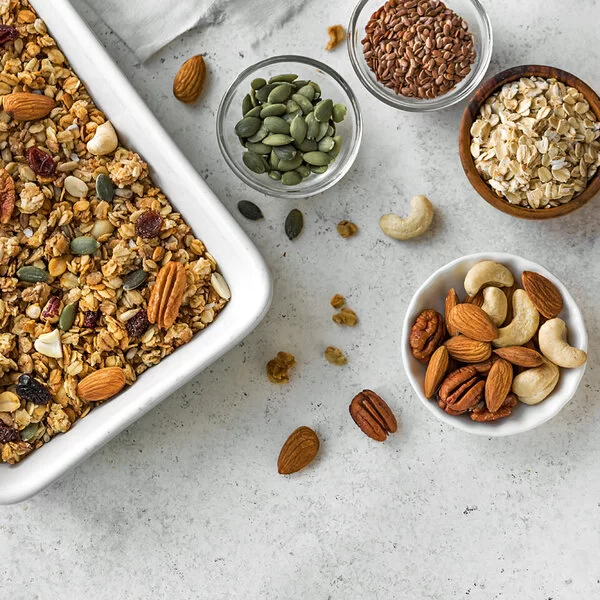 Selbst gemachtes Granola, daneben Zutaten wie Nüsse und Haferflocken.