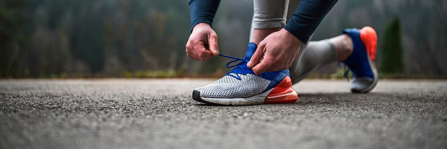 Eine Person bindet sich die Laufschuhe auf Asphalt zu.