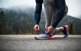 Eine Person bindet sich die Laufschuhe auf Asphalt zu.