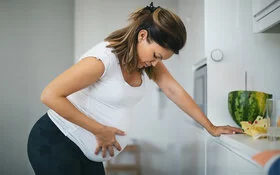 Eine Frau mit Wehen stützt sich auf der Küchenzeile auf und hält sich den Babybauch.