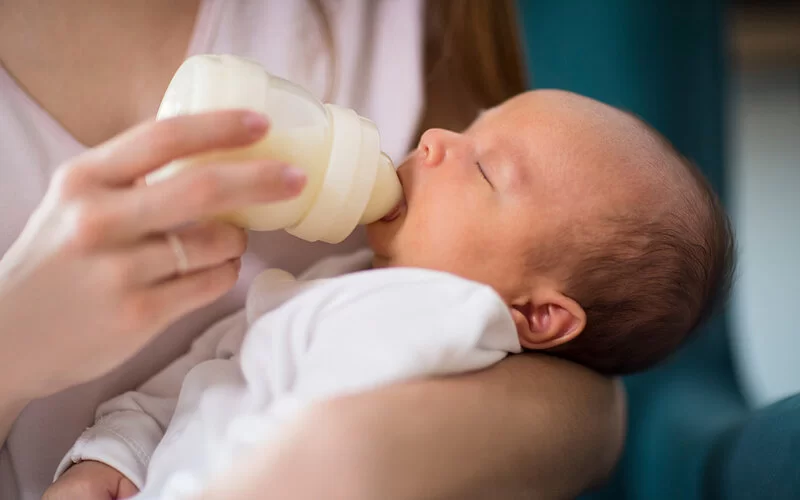 Eine Mutter hält ein Neugeborenes im Arm und gibt ihm die Flasche.