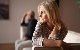 Eine Frau sitzt mit auf einem Sofa. Ein Mann sitzt im Hintergrund.