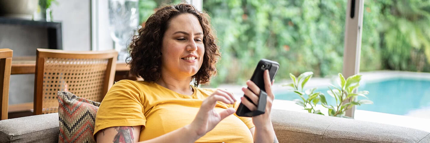 Eine junge mehrgewichtige Frau liegt bequem auf der Couch und surft mit ihrem Smartphone im Internet.